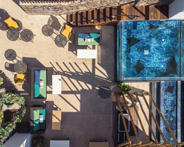 An aerial view of a rooftop pool area with multiple seating arrangements, a large pool, and a wooden deck.
