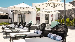 Sillones de exterior con cojines blancos y estructura negra, dispuestos bajo grandes sombrillas blancas.