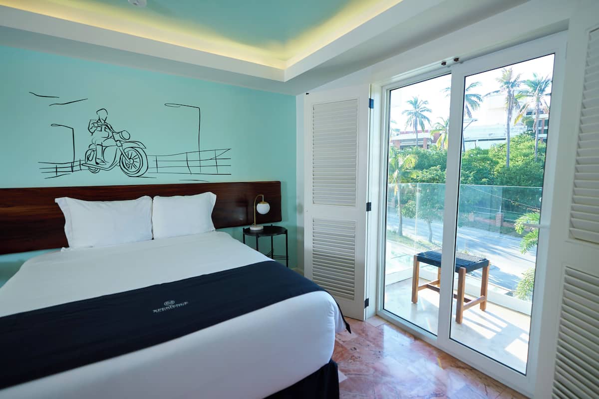 Una habitación de hotel con una cama grande, vista de la calle a través de una puerta corrediza de vidrio y un mural en la pared.