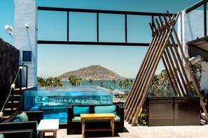 A pool area with a glass enclosure, outdoor seating, and a view of the sea and a mountain.