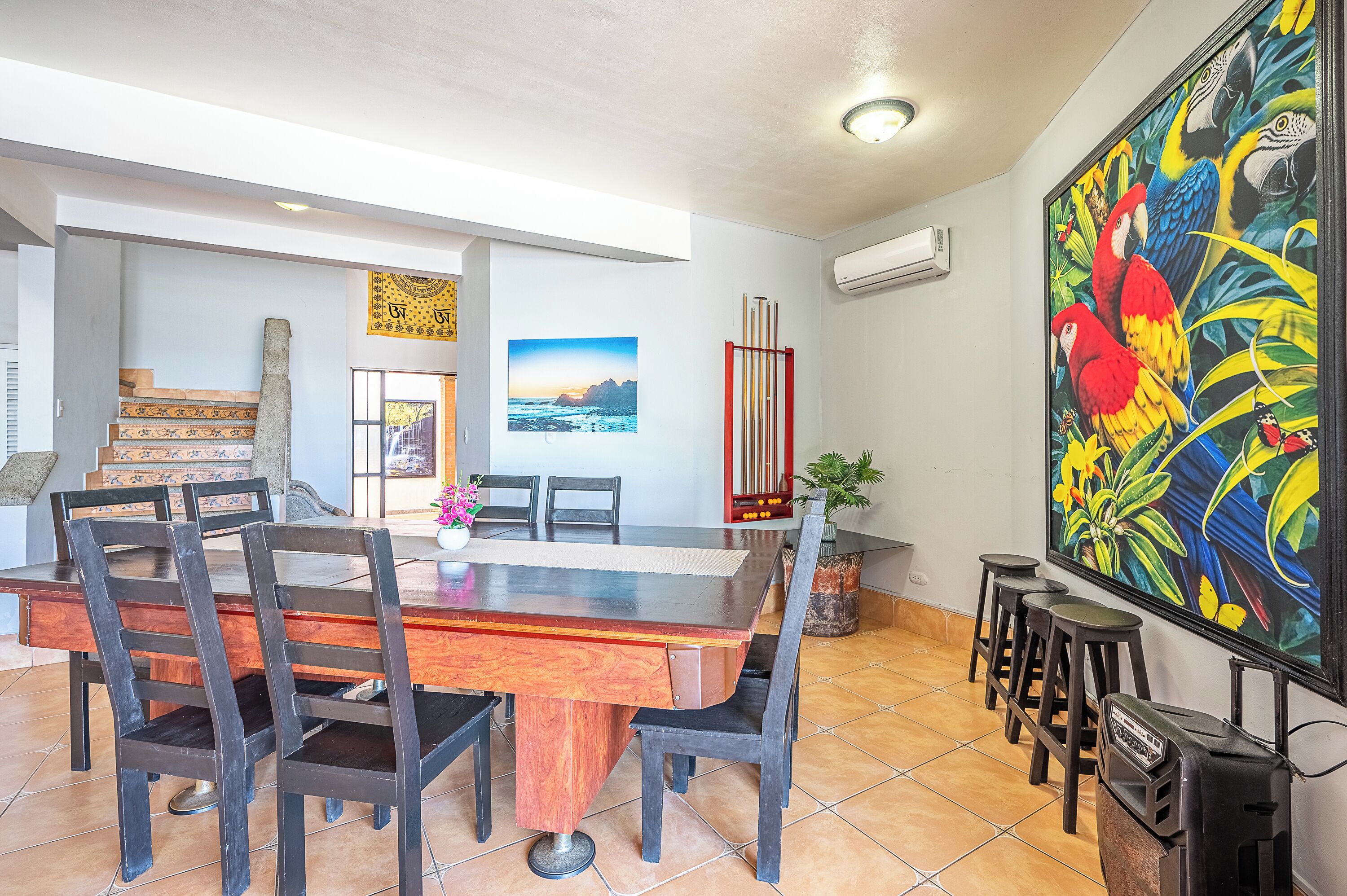 Un comedor con una mesa y sillas de madera, un cuadro grande de guacamayos y un piano rojo.