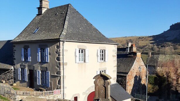 A stone house with a sloped roof, white shutters, and a stone chimney.
