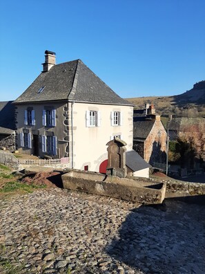 Ein Steinhaus mit geneigtem Dach, weißen Fensterläden und einem Steinkamin.