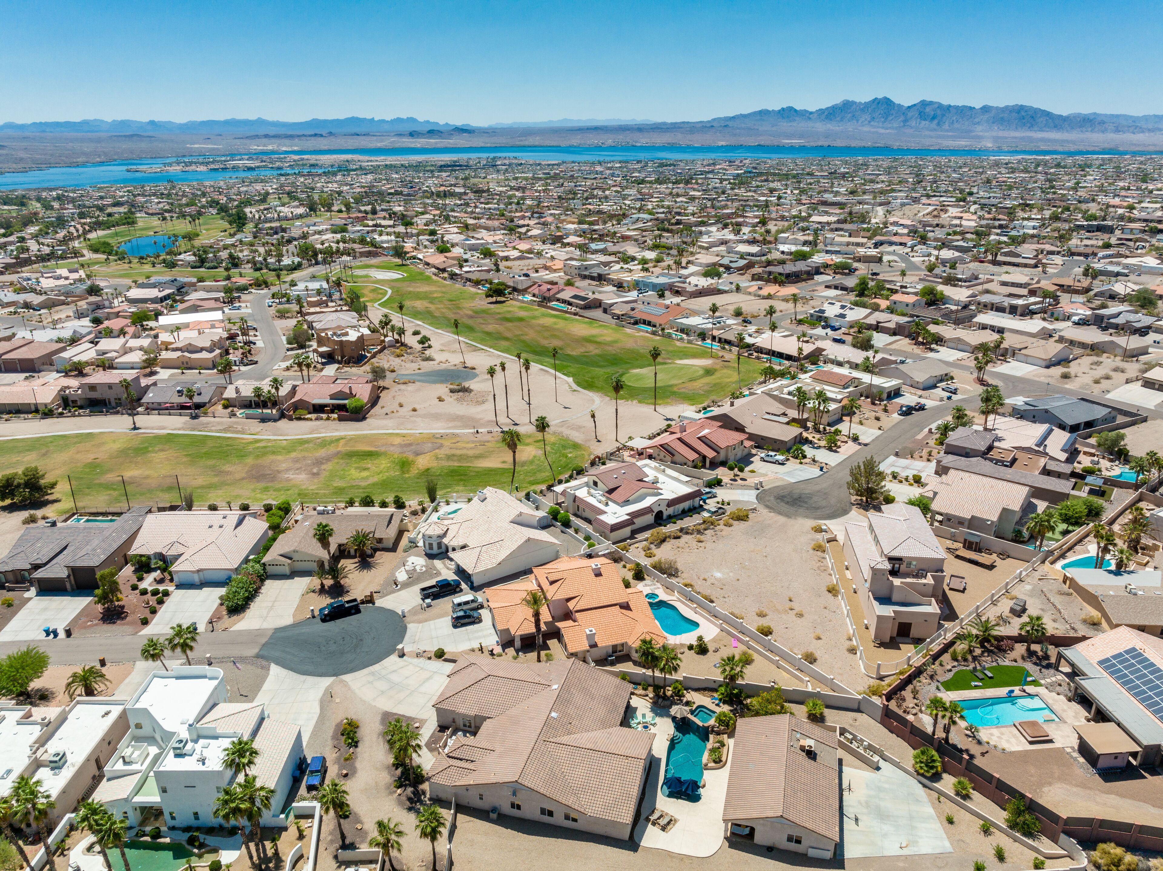 Vista aérea de um bairro residencial com casas, um grande campo verde e uma piscina.