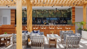Un espace extérieur aménagé avec des chaises et des tables en osier, un bar proposant une grande variété de boissons, et une pergola en bois décorée de guirlandes lumineuses.