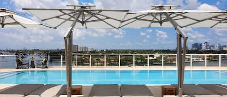 A rooftop pool area with lounge chairs and umbrellas, overlooking a city skyline.