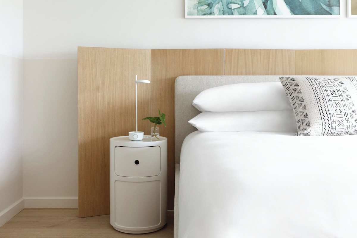 A neatly arranged bedroom with a bed, a bedside table with a lamp, and a small potted plant.