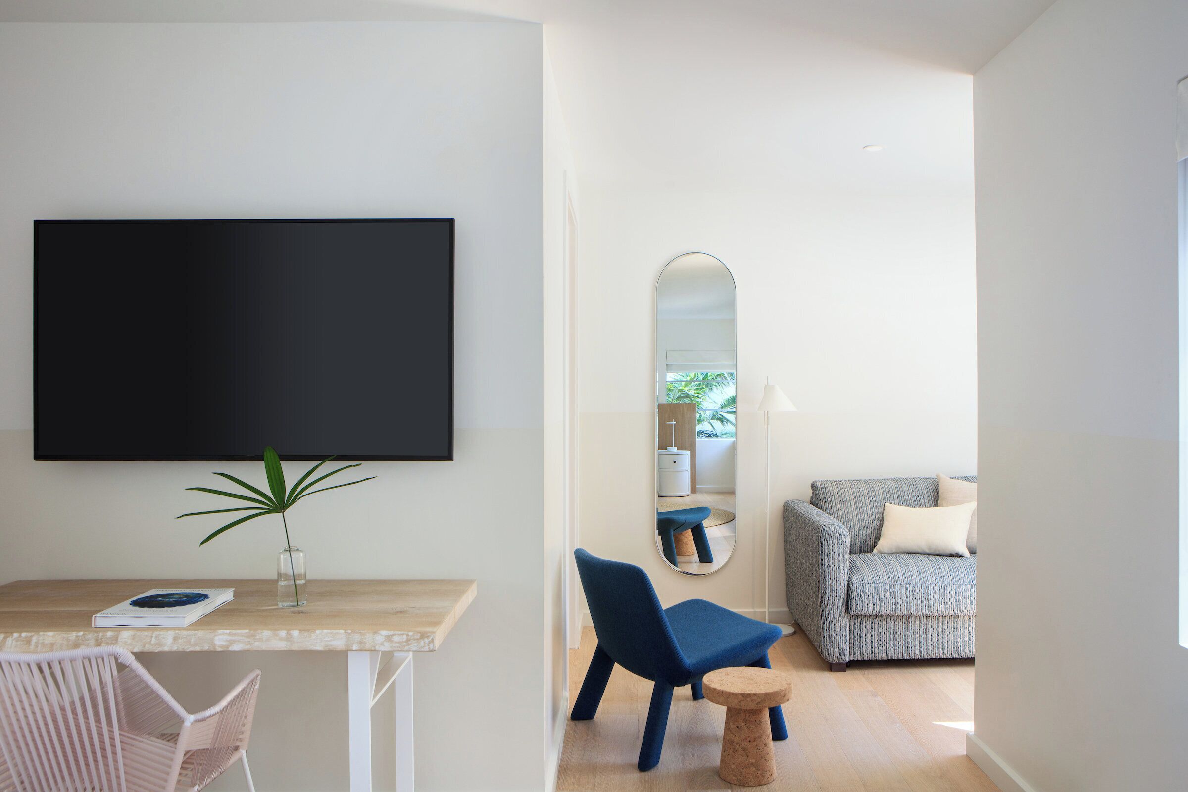 Un salon moderne avec un téléviseur à écran plat, une petite table sur laquelle est posée une plante, un fauteuil bleu, un tabouret rond et un canapé à motifs.