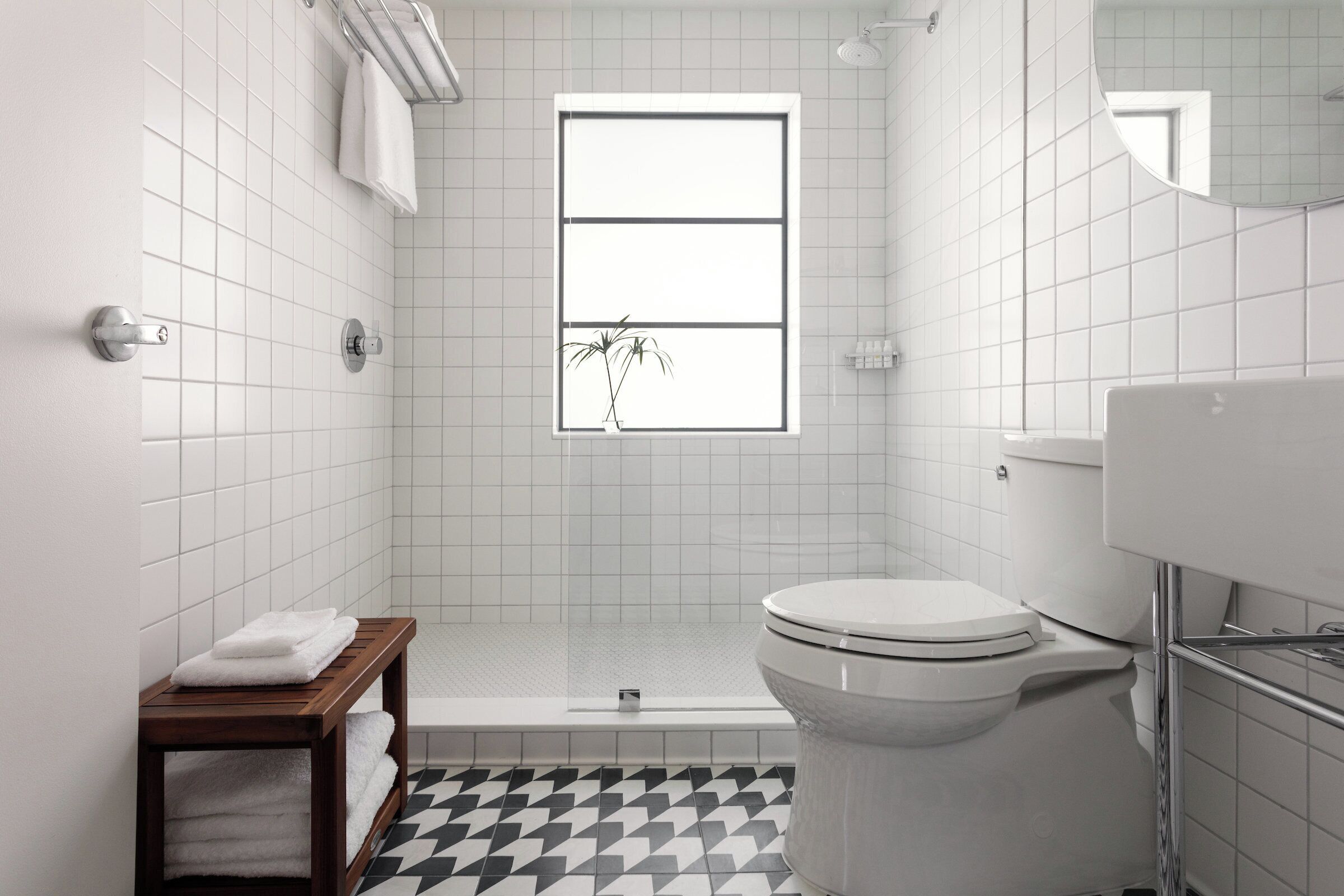 A bathroom with a toilet, a shower, and a sink. There is a window with a view of a plant outside.
