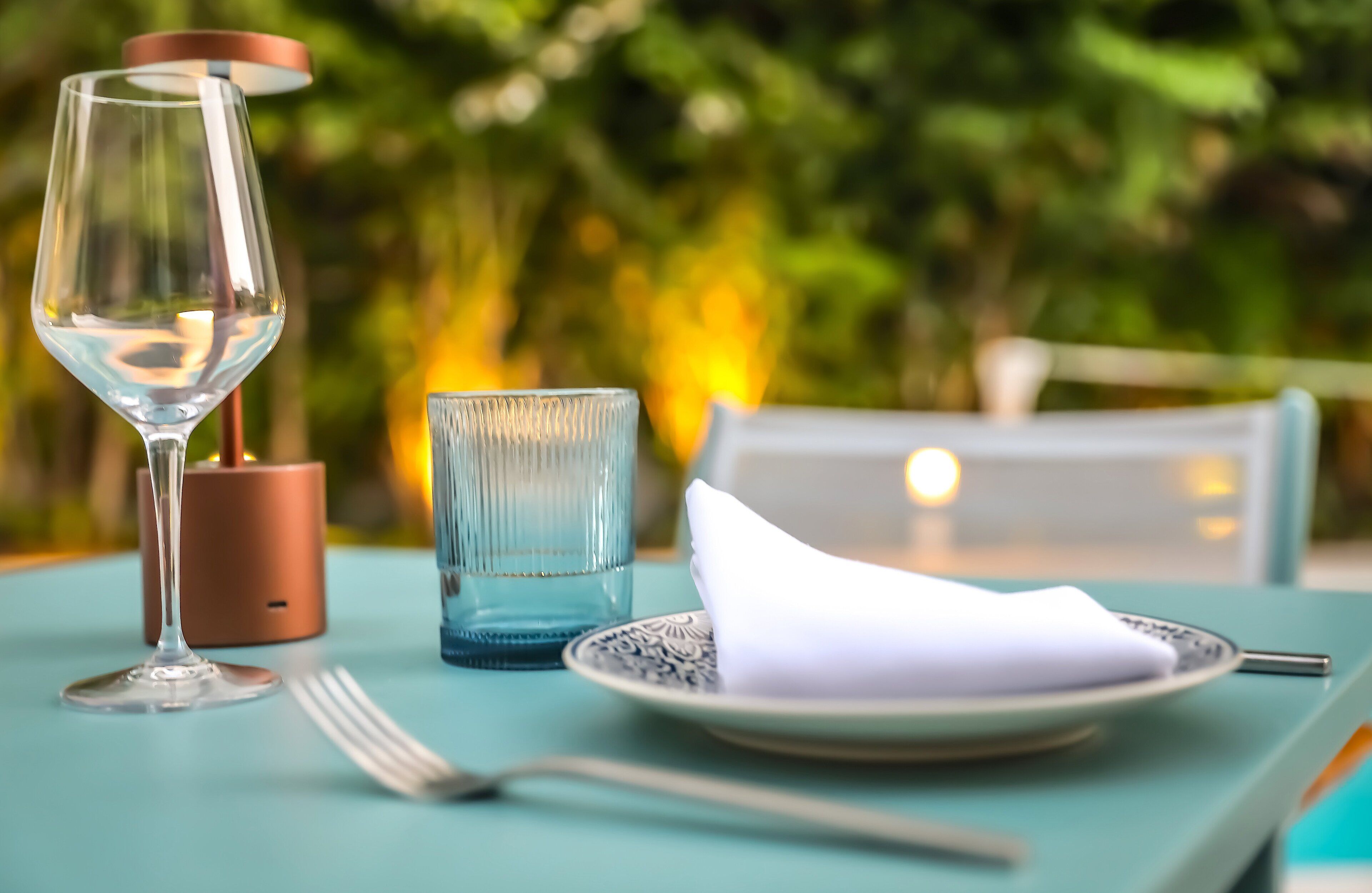 A table set with a wine glass, a blue glass, a plate with a napkin, and cutlery.