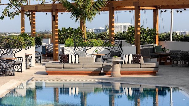 Un área de piscina en la azotea con una pérgola de madera, asientos al aire libre y vistas de la ciudad.