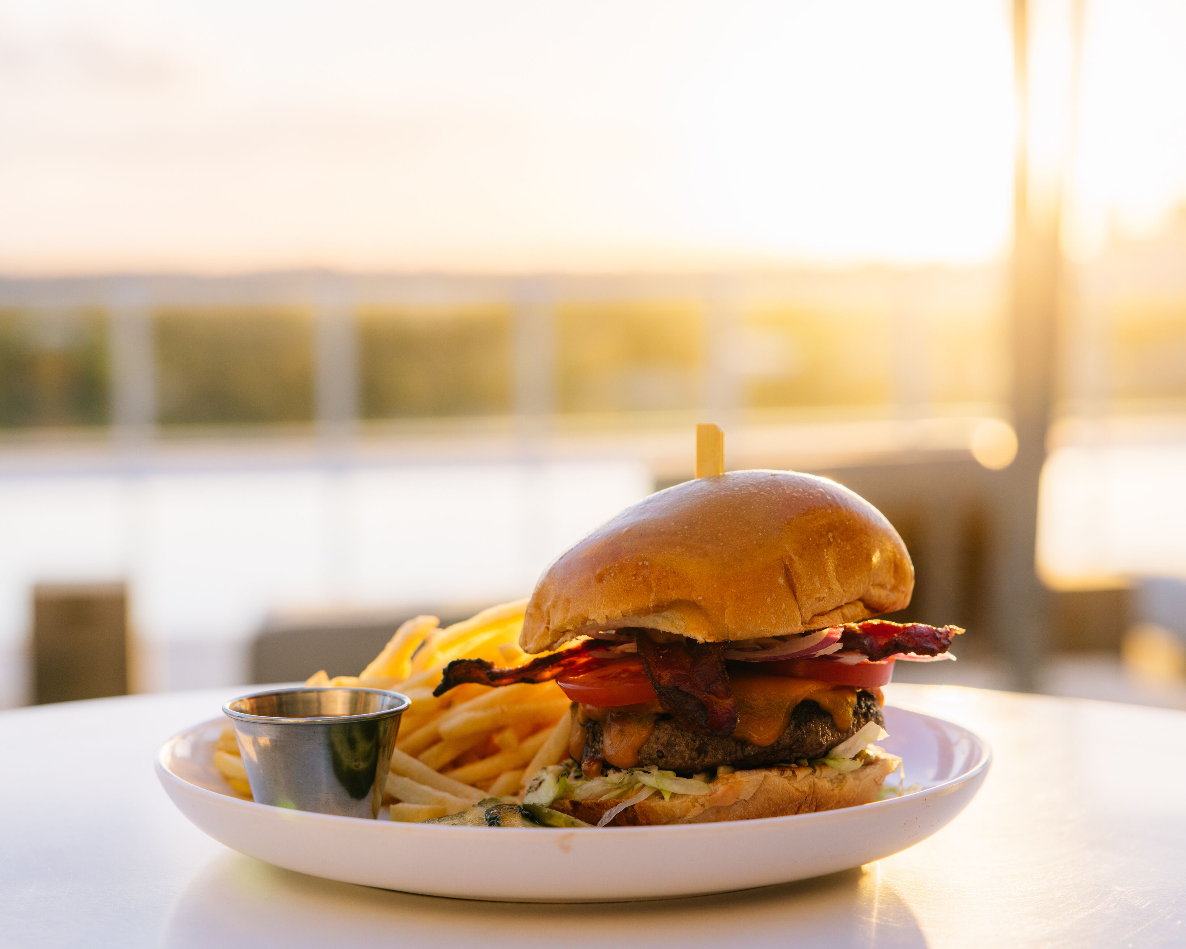 Une assiette contenant un hamburger, des frites et un petit gobelet en métal, posée sur une table.