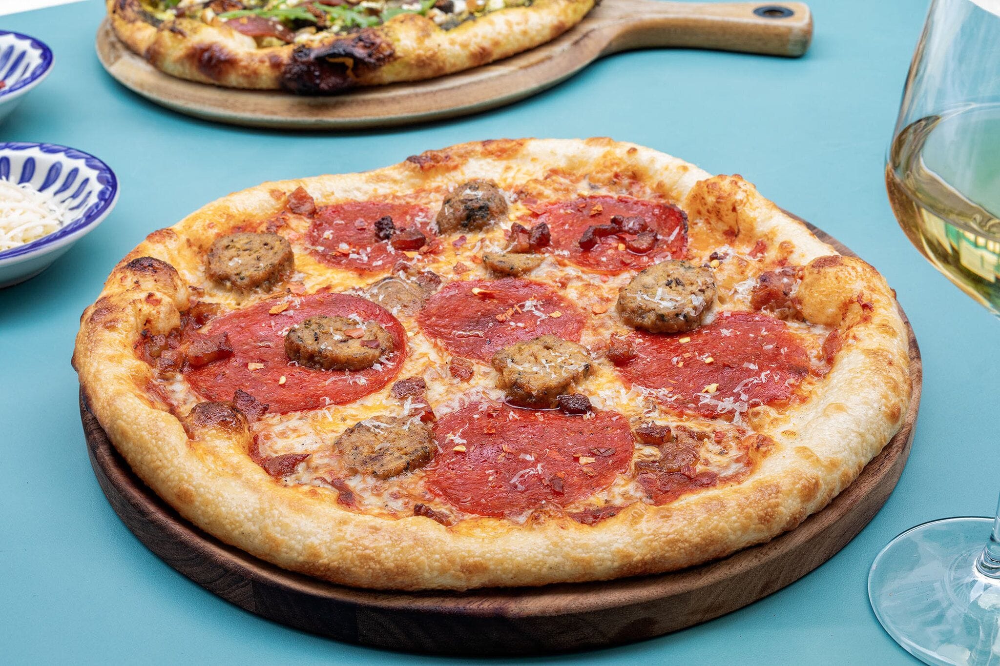 Una pizza con salamino piccante e salsiccia su un tagliere di legno.