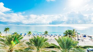 Una playa con palmeras, sombrillas azules y cielo despejado.