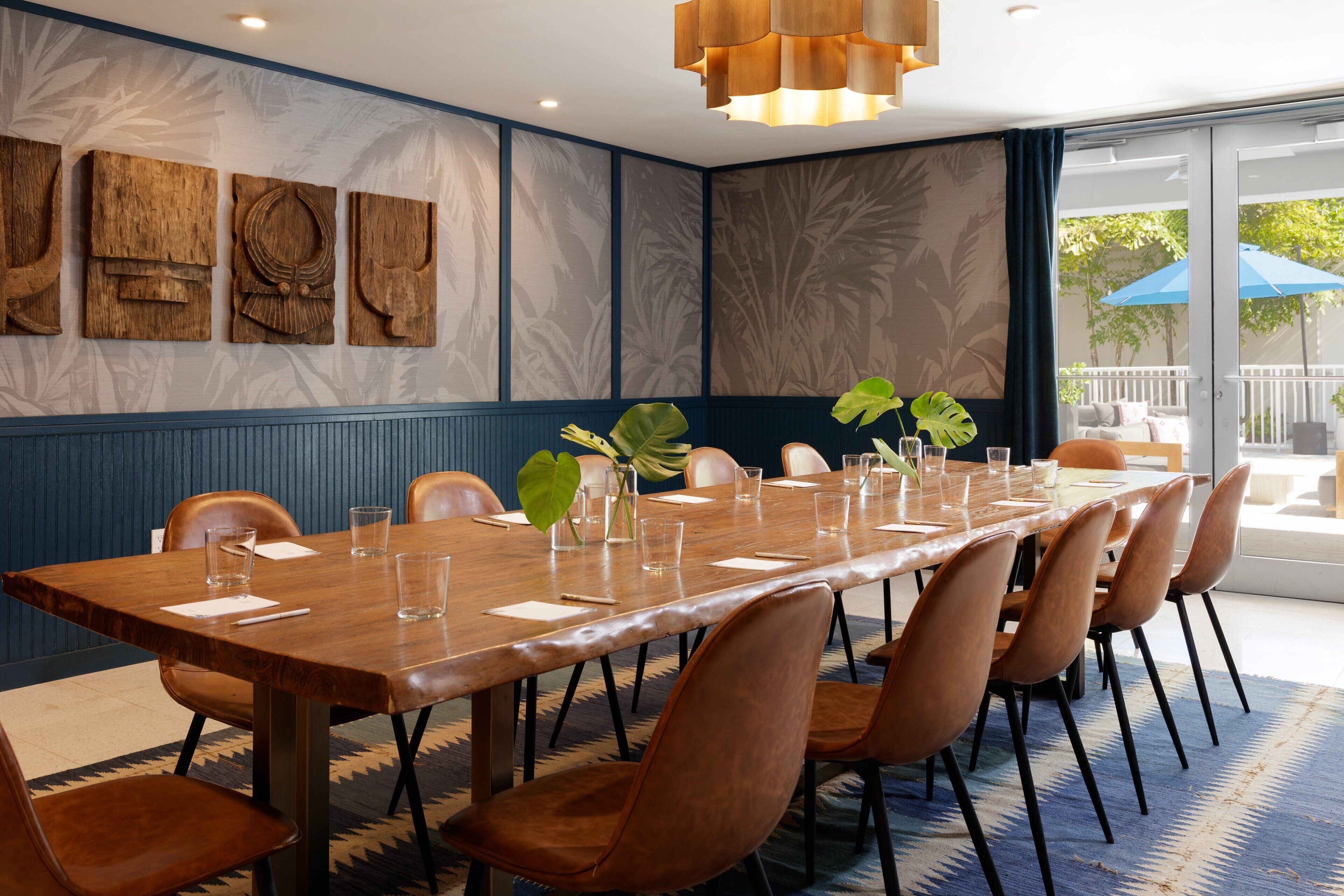 A conference room with a long wooden table, brown leather chairs, and a large window with a view of the outdoors.