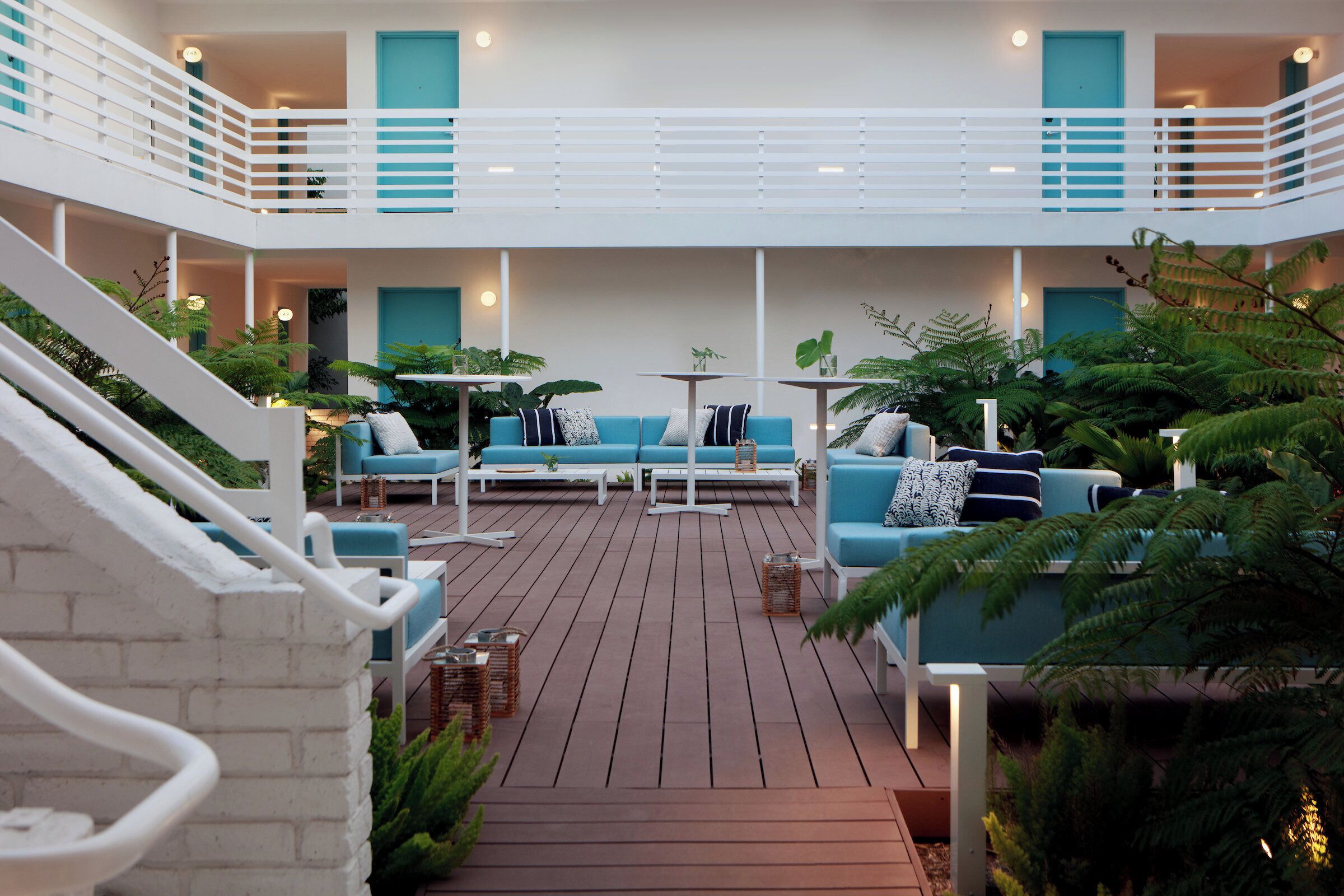 A multi-level outdoor lounge area with blue seating, wooden flooring, and potted plants.