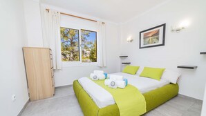A hotel room with a bed, a window with curtains, a bedside table, a wall-mounted light, and a framed picture on the wall.