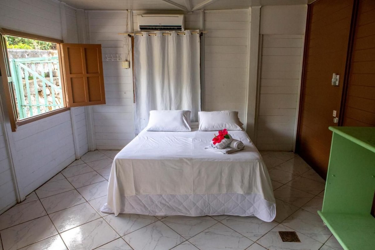 A hotel room with a bed, a window with a curtain, a green cabinet, and a tiled floor.