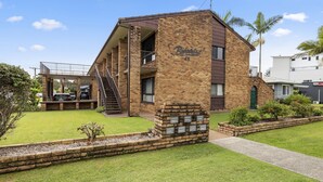 A two-story building with a brick facade, a covered outdoor seating area, and a small garden with palm trees. - Beach Street Bliss - situated in the heart of Woolgoolga (Woolgoolga)