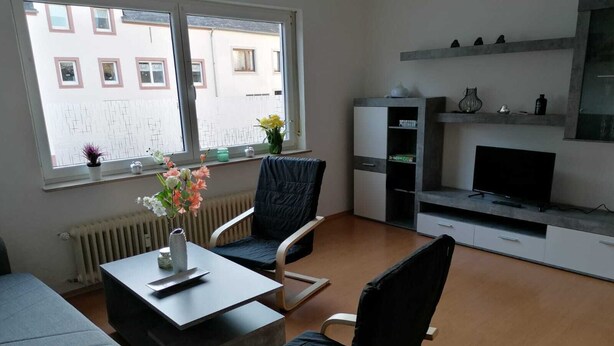 A modern living room with a sofa, two armchairs, a coffee table, a TV, and a radiator. - Ferienwohnung 55 m², 1 Schlafzimmer, 1 Wohnzimmer, 1 Küche, 1 Bad, 1 Flur (Ensch)