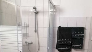A glass-enclosed shower with a handheld showerhead and a wall-mounted towel rack with two towels. - Ferienwohnung 55 m², 1 Schlafzimmer, 1 Wohnzimmer, 1 Küche, 1 Bad, 1 Flur (Ensch)