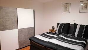 A bedroom with a bed, a nightstand, a lamp, and two framed pictures on the wall. - Ferienwohnung 55 m², 1 Schlafzimmer, 1 Wohnzimmer, 1 Küche, 1 Bad, 1 Flur (Ensch)