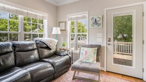 Una sala de estar con un sofá de cuero negro, un sillón gris, una mesita con una lámpara y una puerta que da a una terraza.