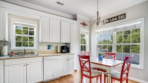 Una cocina con armarios blancos, una mesa de comedor con sillas rojas y vista a árboles a través de ventanas amplias.