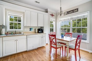 Une cuisine avec des meubles blancs, une table à manger entourée de chaises rouges et une vue sur les arbres, visible à travers de grandes fenêtres.