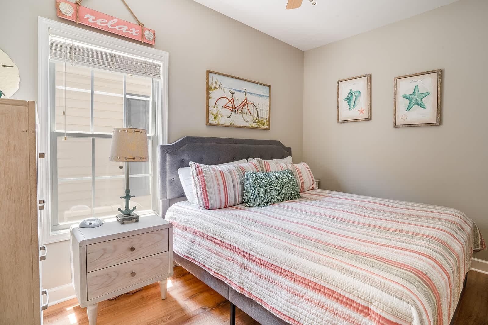 A bedroom with a bed, a nightstand, a lamp, a window with blinds, and wall art.