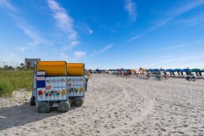 Une plage avec un stand de vente de glaces italiennes, une rangée de chaises de plage et des parasols.