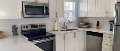 A modern kitchen with white cabinets, stainless steel appliances, and a patterned rug.