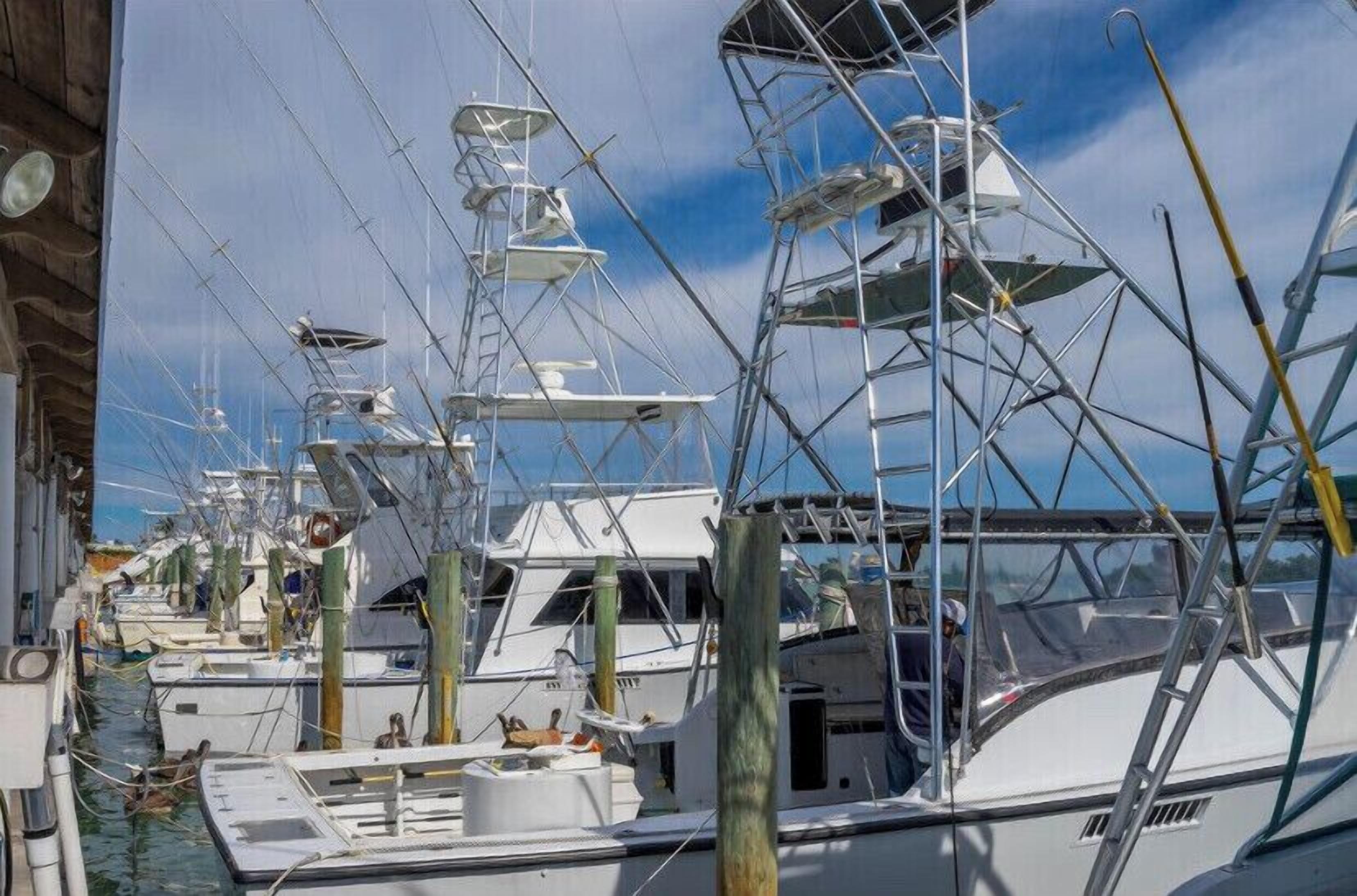 A marina with multiple yachts docked, featuring masts and rigging, and wooden pilings.