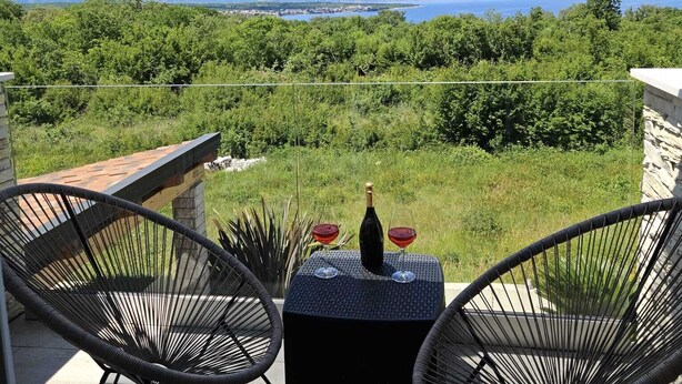 Ein Balkon mit zwei Korbstühlen, einem kleinen Tisch und einer Weinflasche.