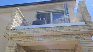 Ein Gebäude mit einer steinernen Fassade, einem Balkon mit Glasgeländer und einem Fenster mit Blick zum Himmel.