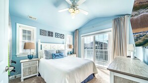 A bedroom with a bed, a nightstand, a dresser, a ceiling fan, and a large window with curtains.