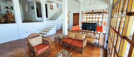 A spacious living area with wicker furniture, a glass coffee table, and a staircase leading to another level.