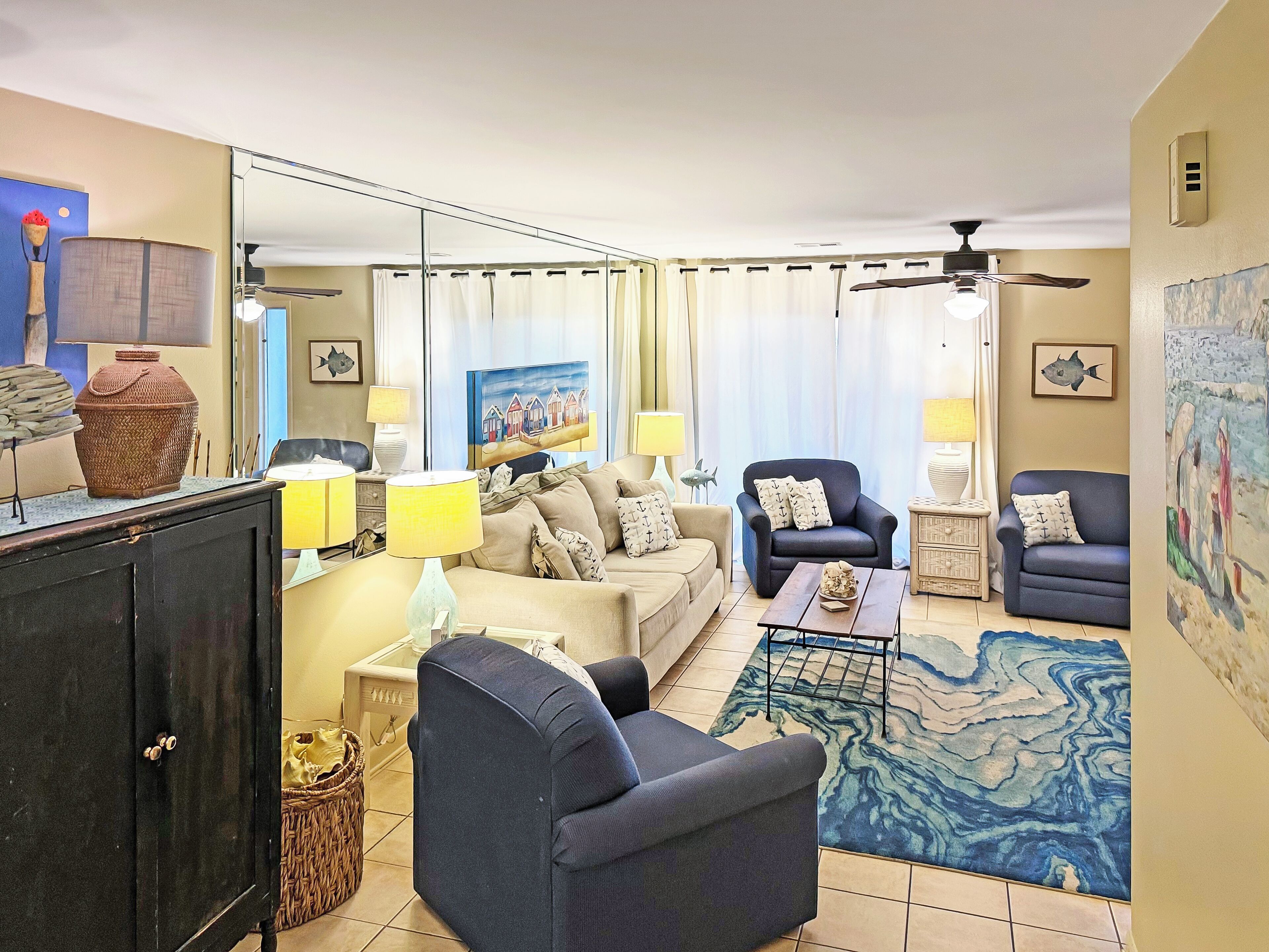 A living room with a sofa, armchairs, a coffee table, and a rug. There is a cabinet, a lamp, and a painting on the wall.