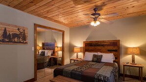 A bedroom with a wooden ceiling, a bed with a wooden headboard, two bedside tables with lamps, a bench, and a mirror. - Grand Panorama - Pet friendly! Sunrise AND Sunset Views, Hot Tub (Banner Elk)