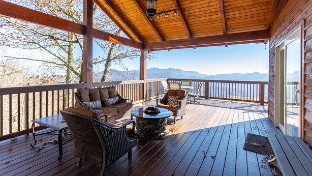 A covered deck with wooden flooring, furnished with wicker chairs and a sofa, overlooking a mountainous landscape. - Grand Panorama - Pet friendly! Sunrise AND Sunset Views, Hot Tub (Banner Elk)