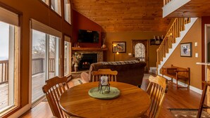 A cozy dining area with a wooden table and chairs, a fireplace, and a staircase leading to an upper level. - Grand Panorama - Pet friendly! Sunrise AND Sunset Views, Hot Tub (Banner Elk)