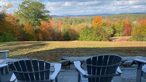 Two Adirondack chairs facing a scenic view of autumn foliage and distant mountains. - Spectacular Views and Sunsets in the Lake Sunapee Region (New London)