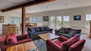 A spacious living area with a wooden coffee table, two sofas, and a dining table. Large windows provide natural light and views of the outdoors. - Spectacular Views and Sunsets in the Lake Sunapee Region (New London)