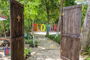 A wooden gate with the word "TEQUILA" spelled out in colorful letters, leading into a garden area with trees and plants.