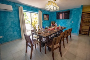A dining area with a wooden table set for six, surrounded by wooden chairs. There is a chandelier above the table, and the room has blue walls.