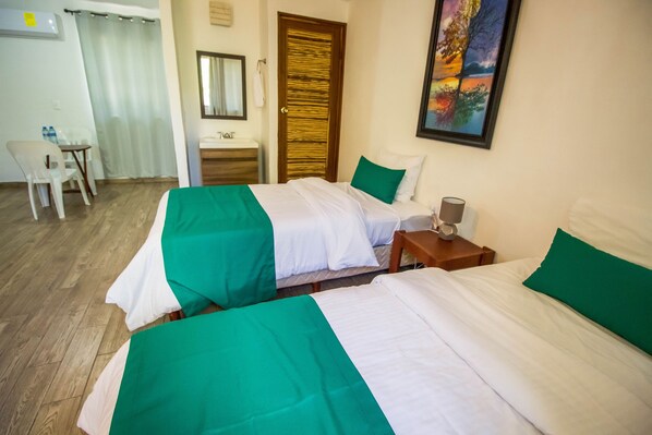 A hotel room with two beds, a desk, a chair, a bathroom, and a painting on the wall.