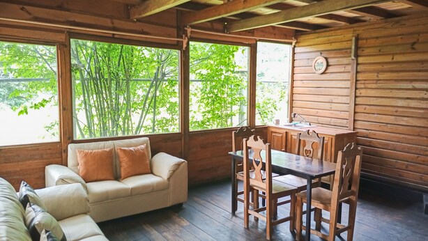 A cozy cabin with a wooden interior, a sofa, a dining table with chairs, and large windows offering a view of greenery outside. - Calkiní Cabañas (San Cristóbal de las Casas)