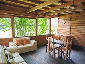 Una cabaña acogedora con interior de madera, un sofá, una mesa de comedor con sillas y ventanas amplias que ofrecen vistas al follaje exterior.
