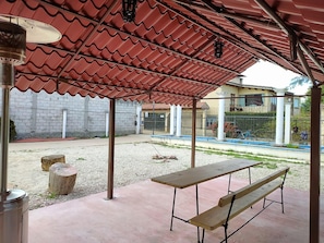 Un patio al aire libre con techo de tejas rojas, una mesa de concreto y bancos.