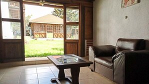 A room with a brown leather sofa, a glass-top coffee table, and a view of a house through large windows. - Calkiní Cabañas (San Cristóbal de las Casas)